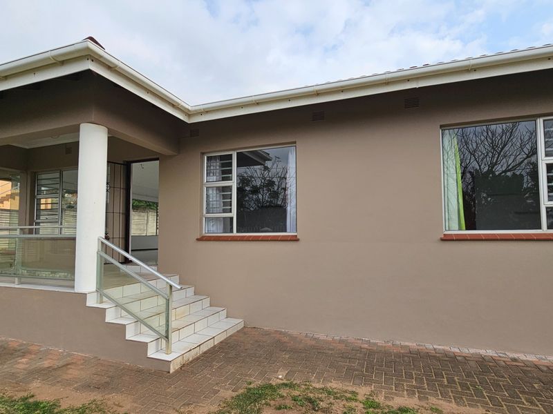 Rear exterior view of the house featuring a covered patio, tiled steps with a modern glass balustrade, and paved outdoor area.