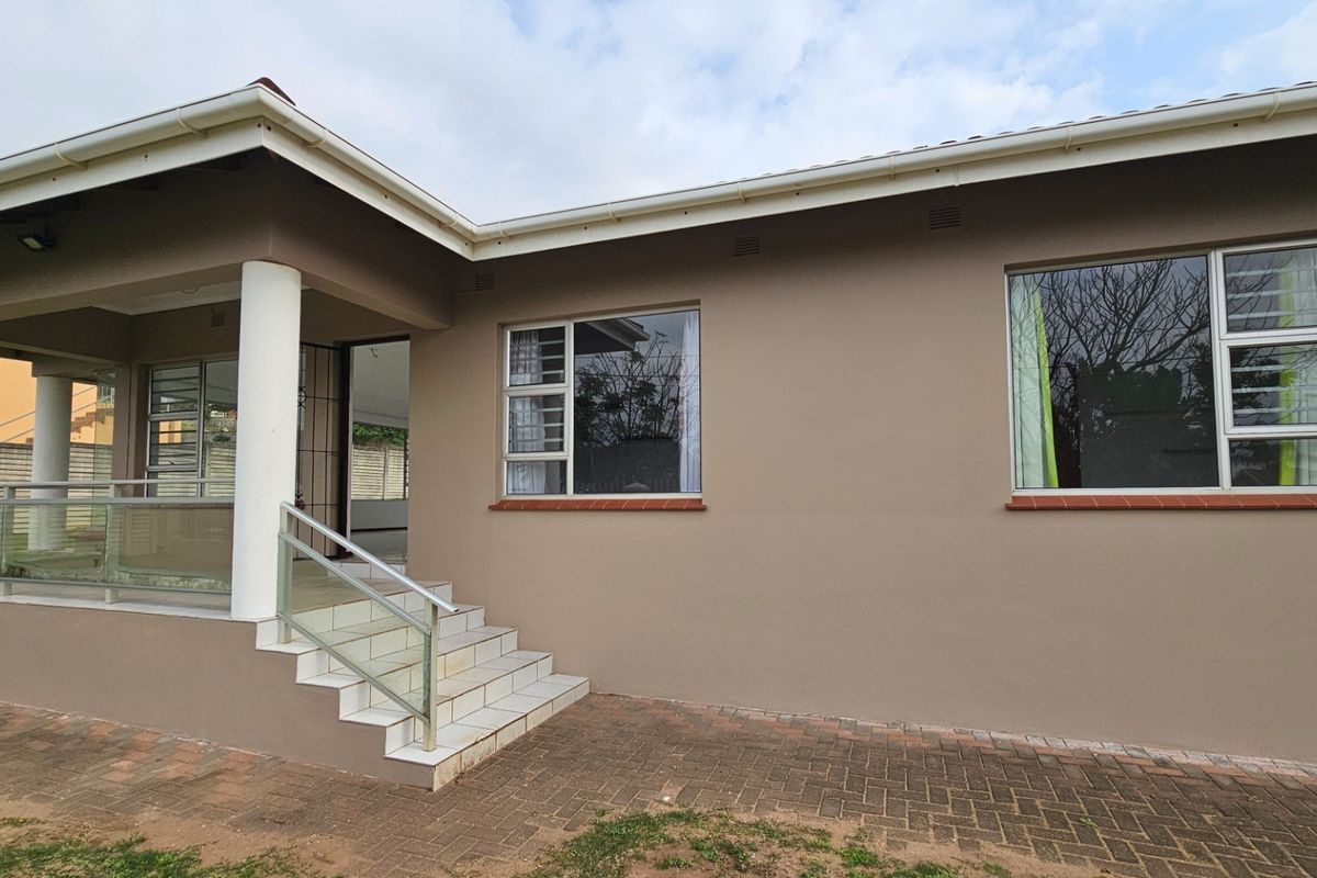 Rear exterior view of the house featuring a covered patio, tiled steps with a modern glass balustrade, and paved outdoor area.