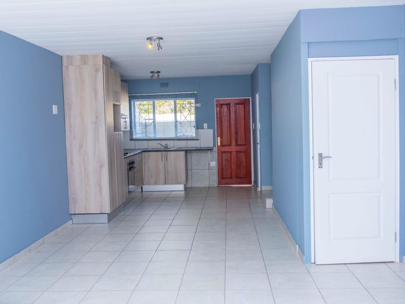 Open plan living area featuring tiled flooring, blue painted walls, and a compact kitchen with built-in cabinetry and a timber entrance door.