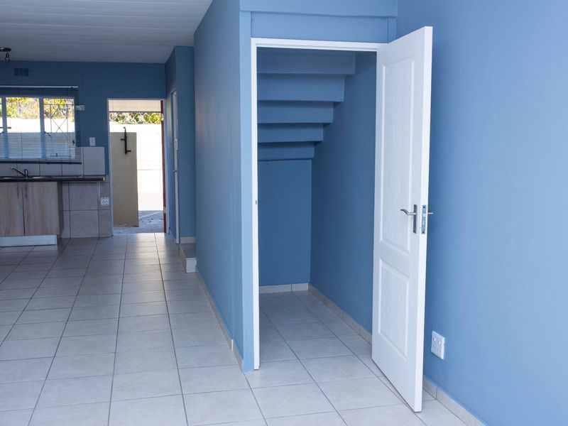 Open plan living area featuring tiled flooring, blue painted walls, and convenient under-stair storage space, leading through to a functional kitchen area.