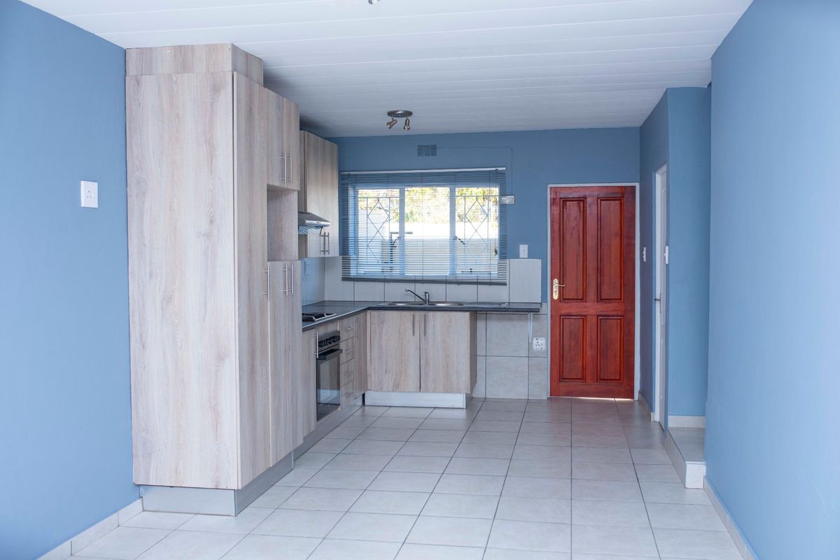 A clean, functional kitchen featuring light wood-look cabinetry, built-in oven and hob, tiled flooring, and a secure window overlooking the exterior.