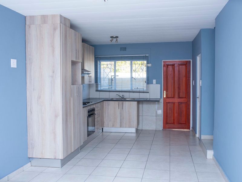 A clean, functional kitchen featuring light wood-look cabinetry, built-in oven and hob, tiled flooring, and a secure window overlooking the exterior.