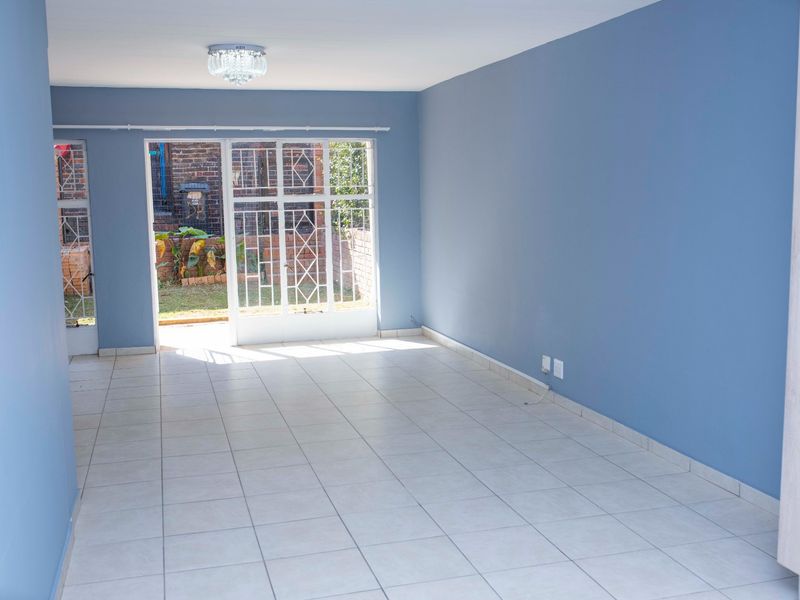 A bright, empty living room featuring tiled flooring, blue painted walls, and a security gate leading to an outdoor area.