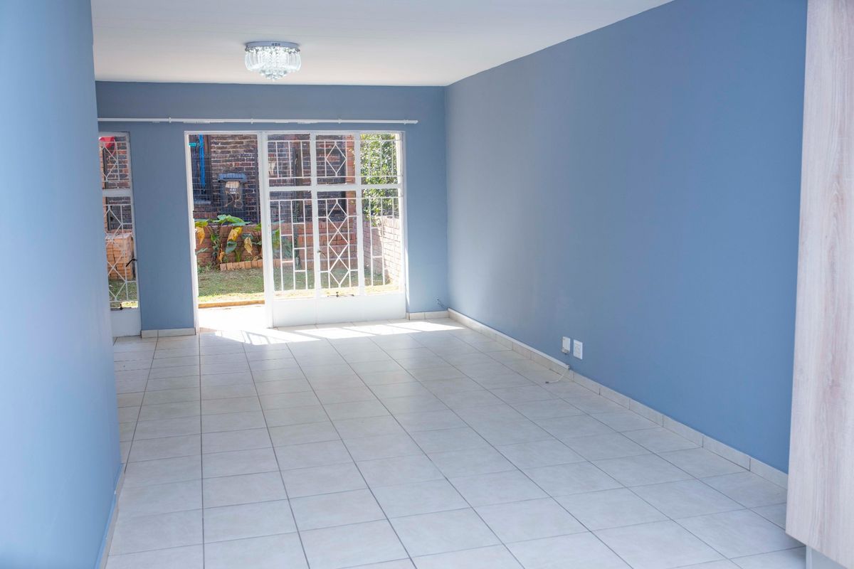 A bright, empty living room featuring tiled flooring, blue painted walls, and a security gate leading to an outdoor area.