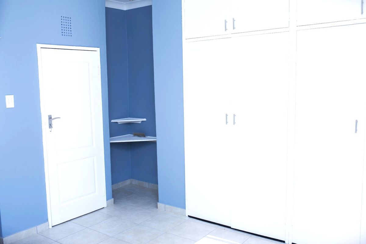 A bedroom featuring built-in cupboards, corner shelving, and tiled flooring, finished with blue painted walls.