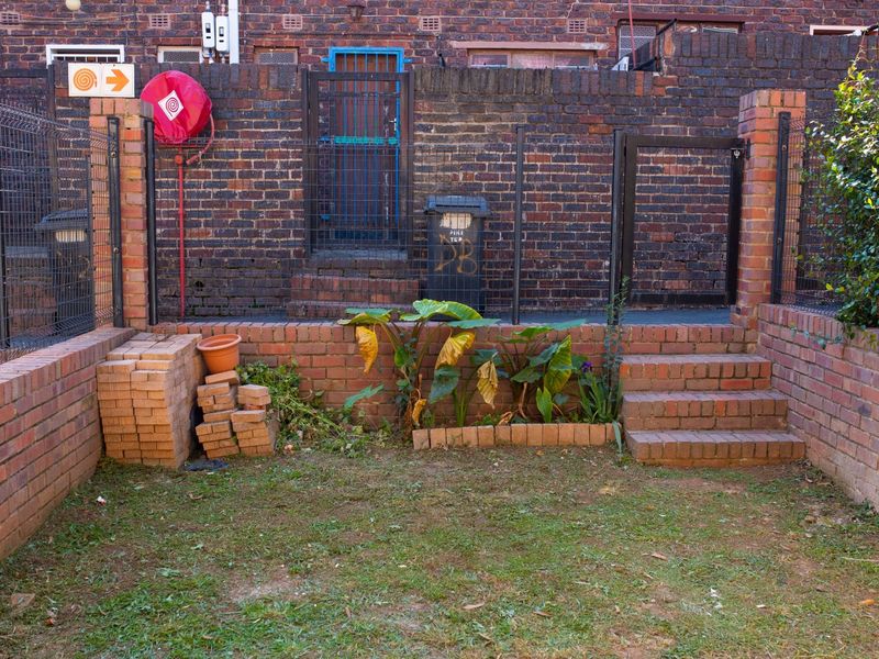 A small rear courtyard area featuring brick retaining walls, stairs, and a metal security gate, providing a functional outdoor space.