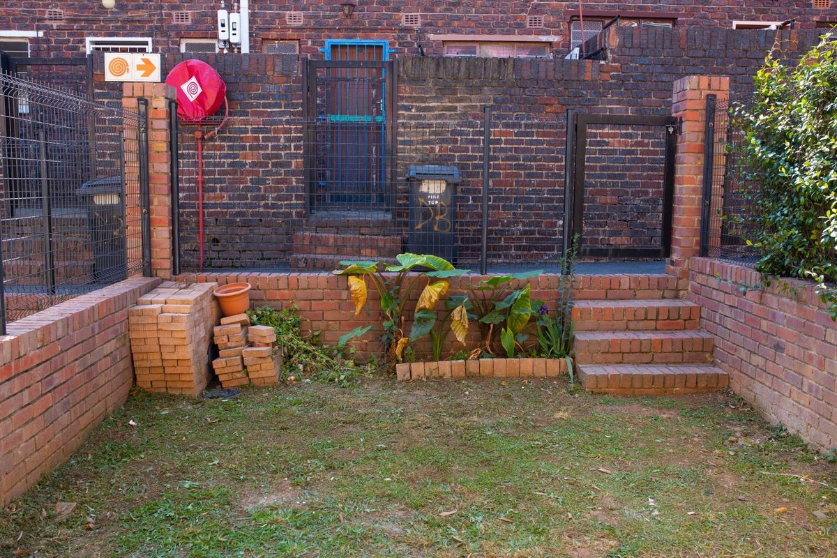 A small rear courtyard area featuring brick retaining walls, stairs, and a metal security gate, providing a functional outdoor space.
