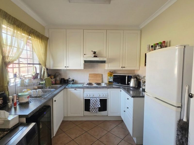 A functional kitchen featuring white cabinetry, laminate countertops, an electric stove with extractor fan, and tiled flooring.