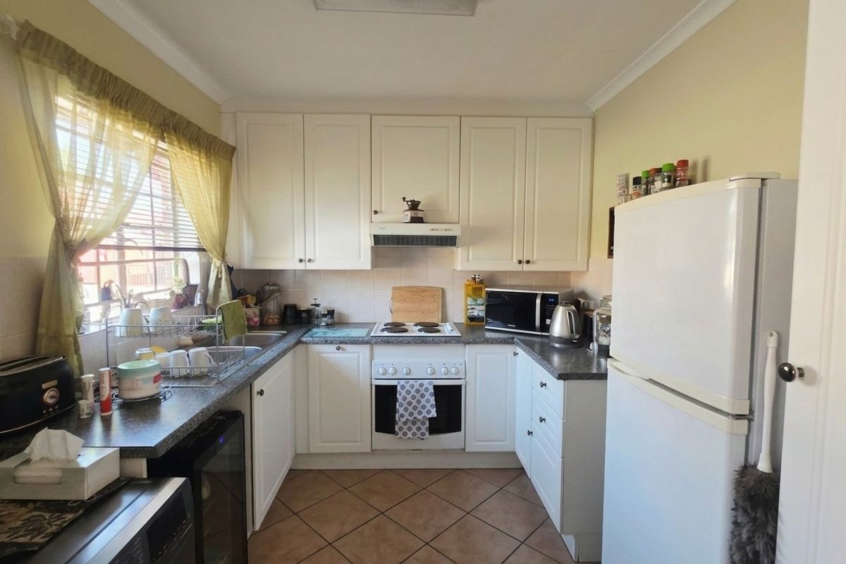 A functional kitchen featuring white cabinetry, laminate countertops, an electric stove with extractor fan, and tiled flooring.