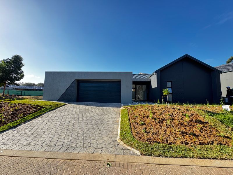 Modern front elevation featuring a paved driveway, automated garage, and contemporary dark exterior finishes with newly landscaped garden beds.