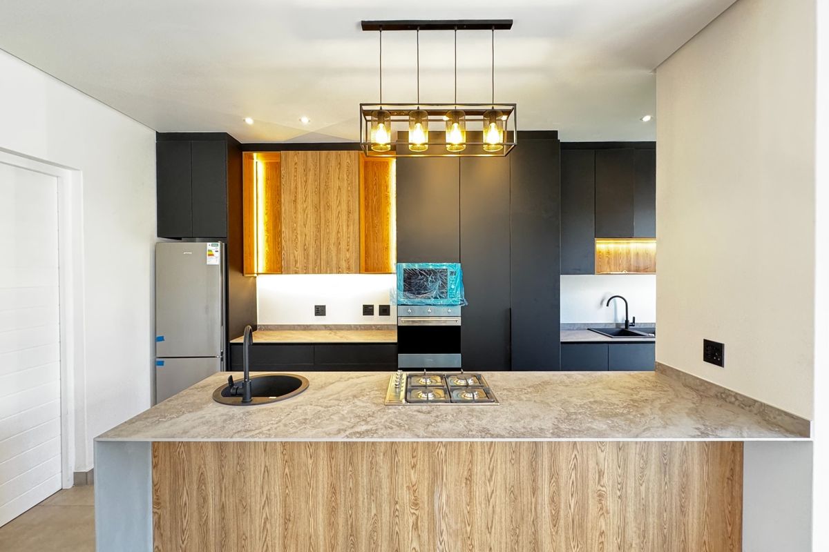 Modern kitchen featuring a central island with gas hob, stone countertops, matte black fixtures, and sleek two-tone cabinetry with integrated lighting.