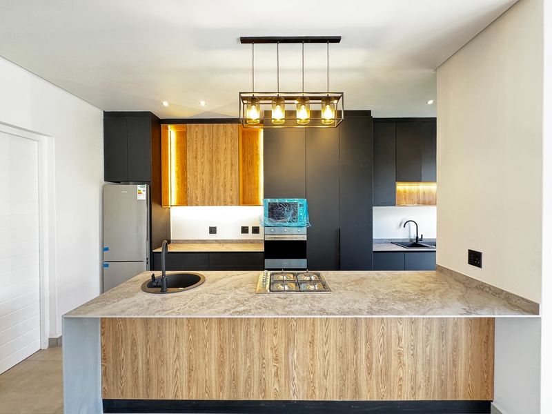 Modern kitchen featuring a central island with gas hob, stone countertops, matte black fixtures, and sleek two-tone cabinetry with integrated lighting.