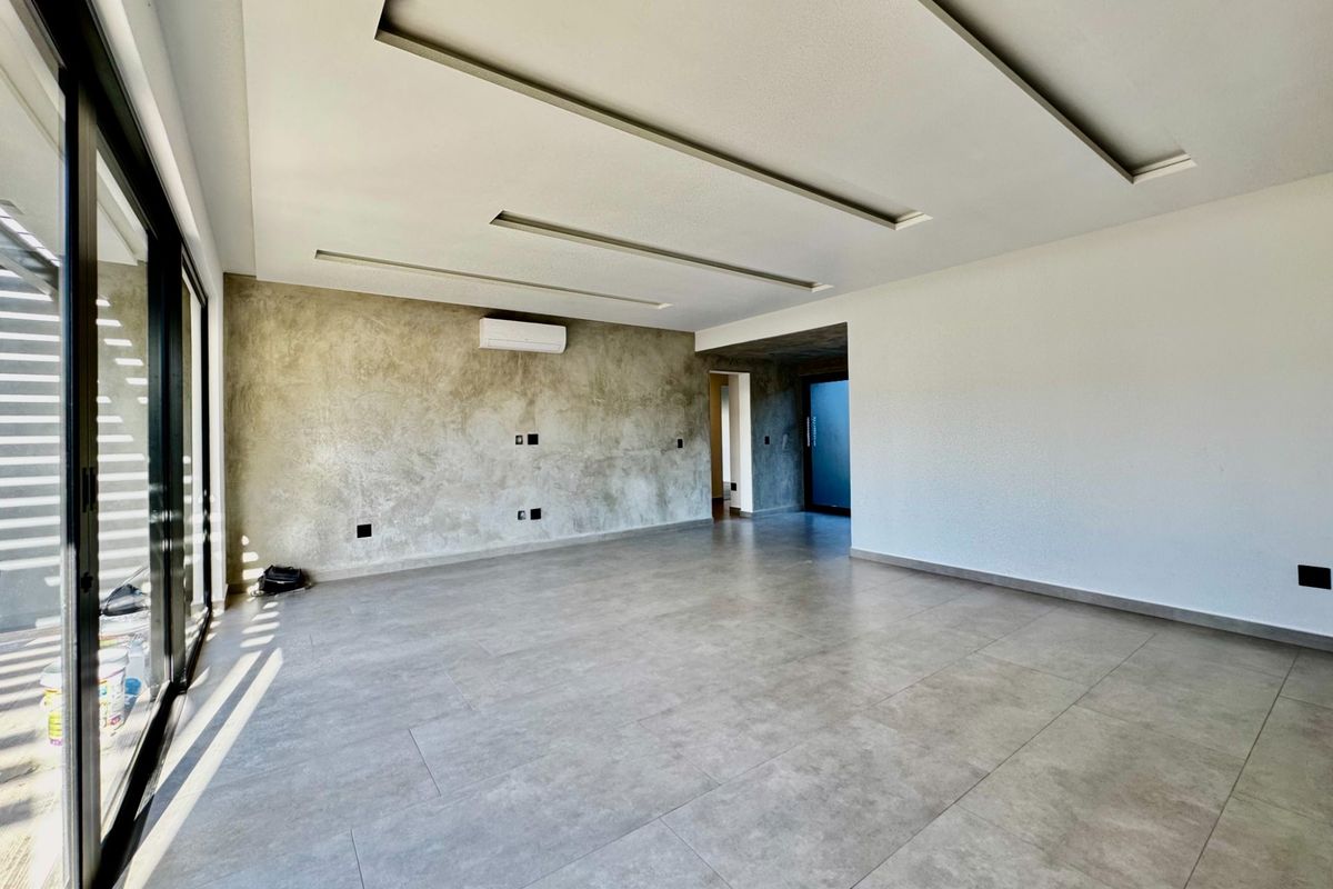 Spacious, modern living area featuring large format floor tiles, a concrete-finish feature wall, recessed ceiling lighting, and sliding glass doors leading to the exterior.