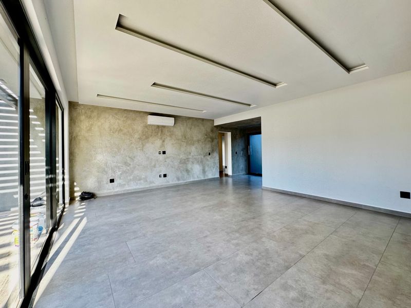 Spacious, modern living area featuring large format floor tiles, a concrete-finish feature wall, recessed ceiling lighting, and sliding glass doors leading to the exterior.