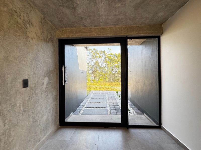 Modern entrance foyer featuring a polished concrete ceiling, textured wall finish, and a large glass sliding door opening onto a paved garden walkway.
