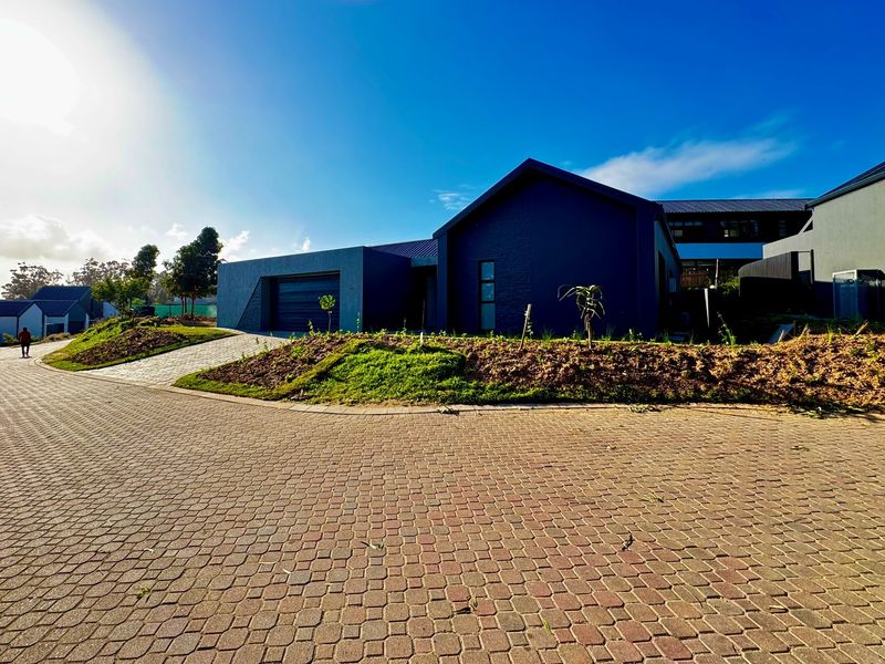 Modern residential property featuring a dark brick facade, integrated garage, and a paved driveway with landscaped garden beds.