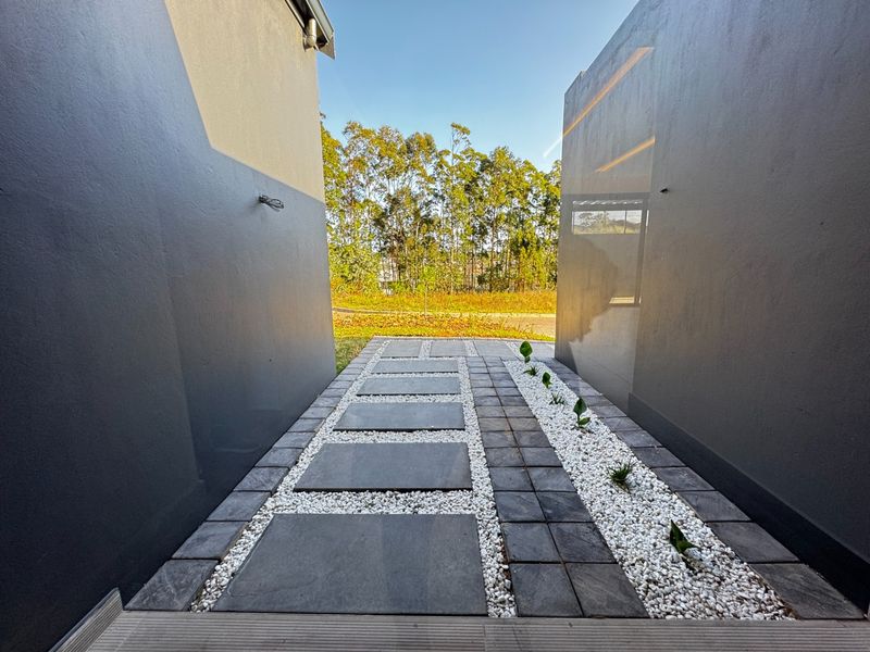 A modern, well-maintained outdoor walkway featuring stone pavers, decorative white gravel, and clean, dark-painted exterior walls leading toward a landscaped garden area.