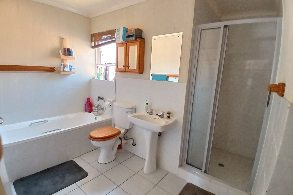 A functional bathroom featuring a bathtub, separate shower enclosure, pedestal basin, and toilet with neutral wall and floor tiling.