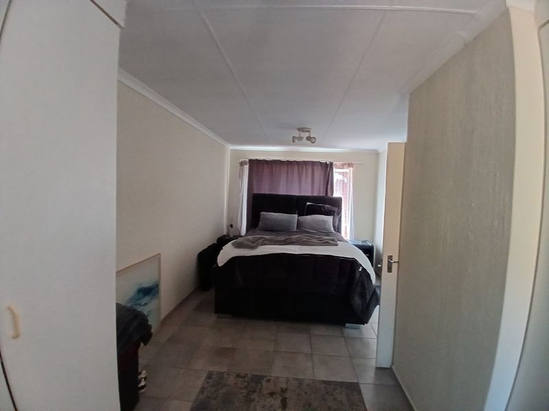 A standard bedroom featuring tiled flooring, built-in cupboards, and neutral wall finishes, providing a functional sleeping space.