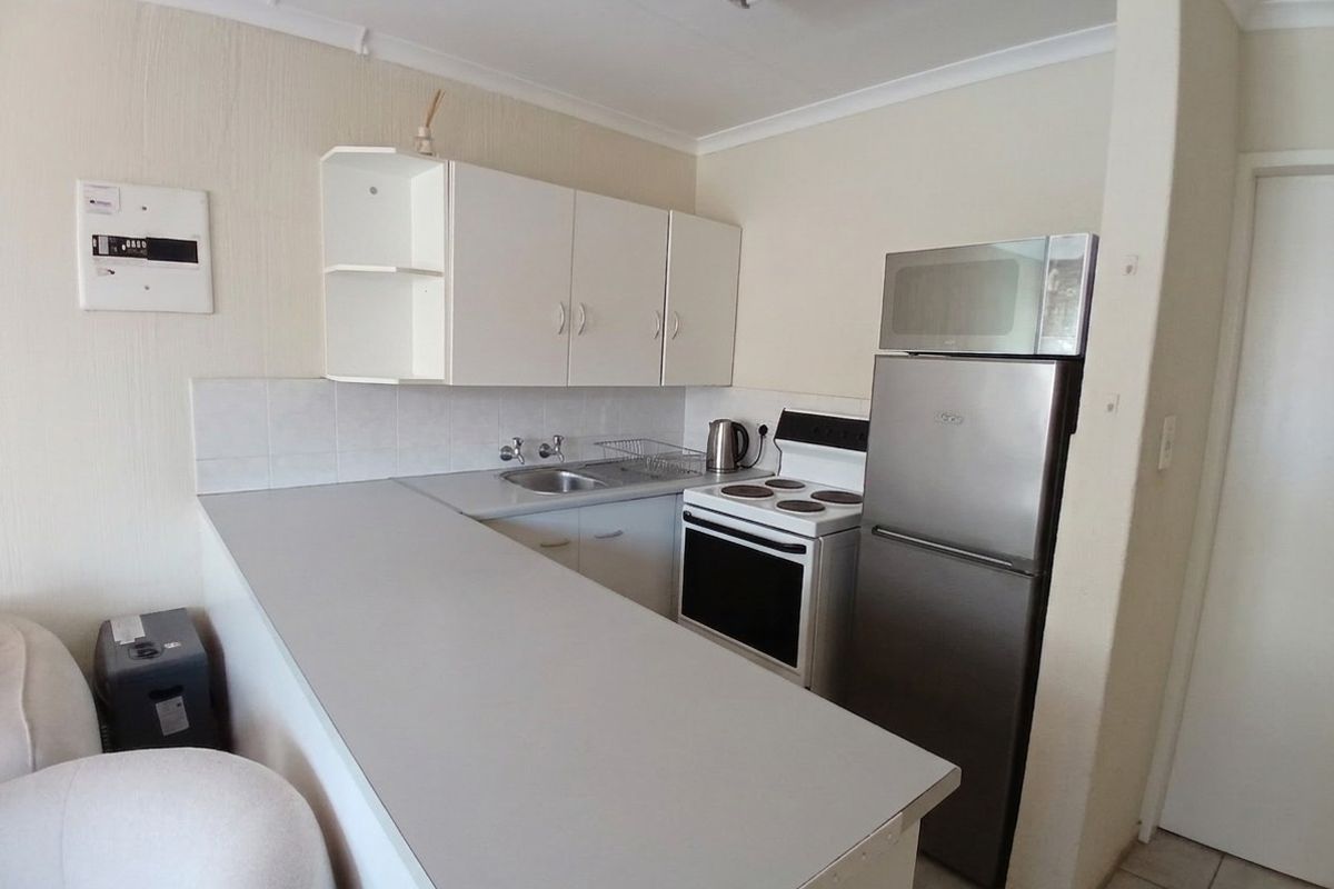 Compact kitchen featuring white cabinetry, laminate countertops, a stainless steel sink, and a freestanding stove, offering a functional layout for a townhouse.
