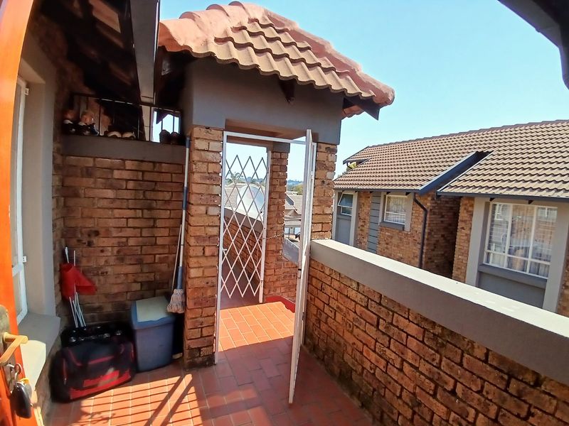 An elevated balcony area featuring exposed brickwork, terracotta tiling, and a security gate, offering an outdoor space with views of the surrounding townhouse complex.