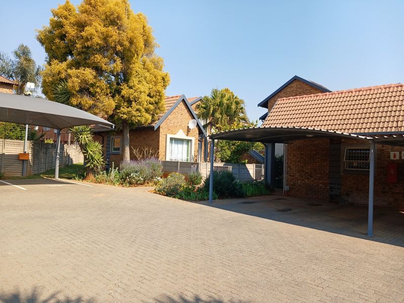 Front exterior view of the townhouse complex featuring brick facades, tiled roofing, and covered carport parking spaces with a paved driveway.