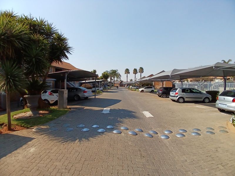 A view of the complex driveway featuring paved surfaces, designated parking bays with shade-cloth carports, and installed speed bumps.