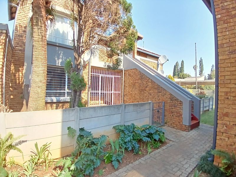 Front exterior view of a face-brick townhouse featuring a paved walkway, security gate, and external staircase access.