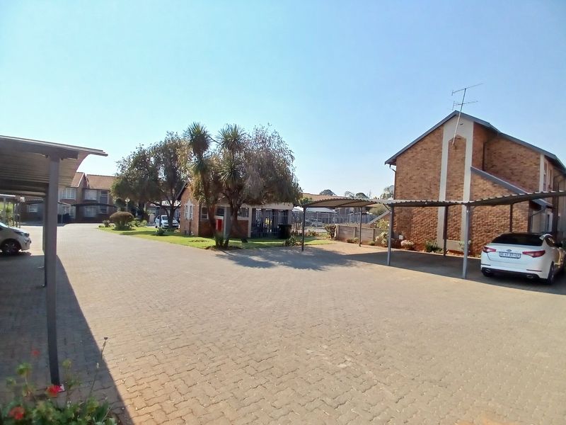 Exterior view of the townhouse complex featuring paved driveways, covered carport parking bays, and established brick building facades.