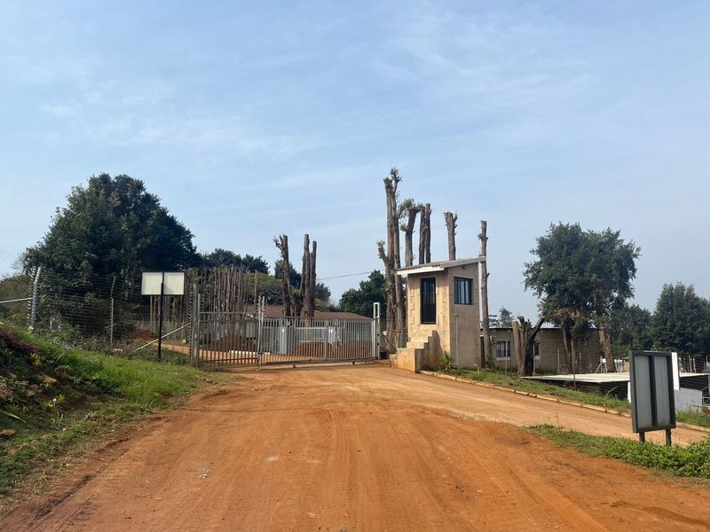 View of the property entrance featuring a security gate, guard house, and perimeter fencing accessible via a dirt road.