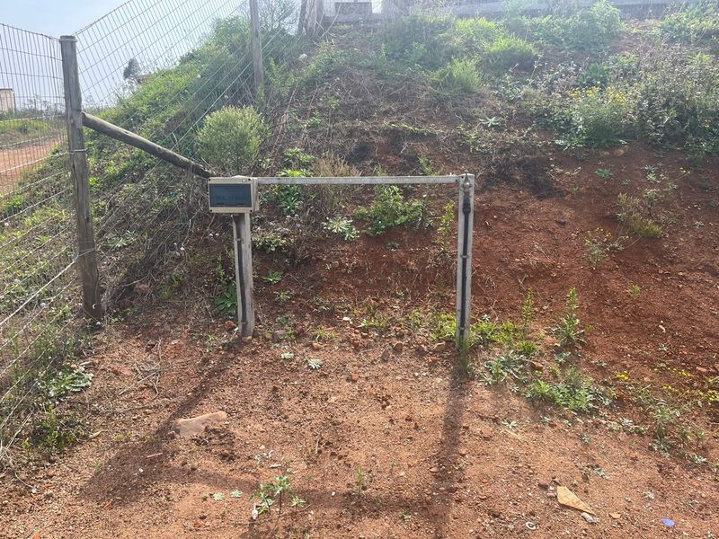 A view of the property boundary featuring wire mesh fencing and a utility connection point set against an undeveloped, sloped earth bank.