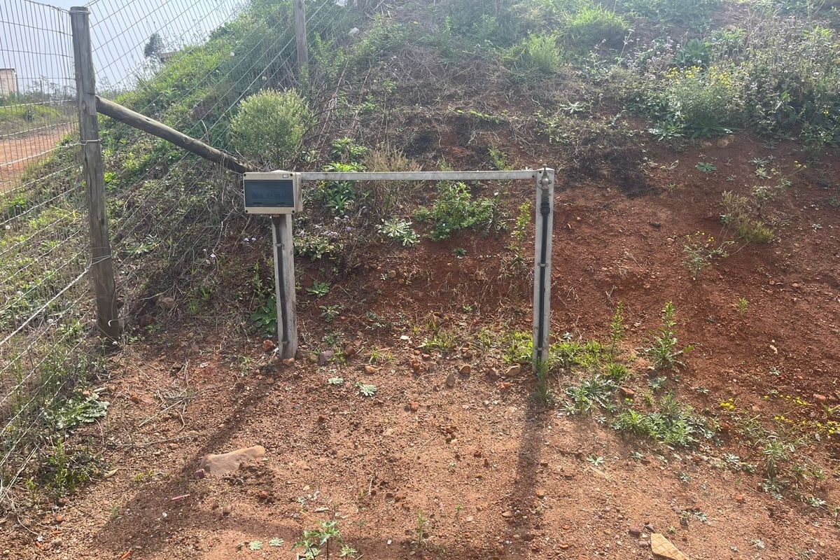 A view of the property boundary featuring wire mesh fencing and a utility connection point set against an undeveloped, sloped earth bank.
