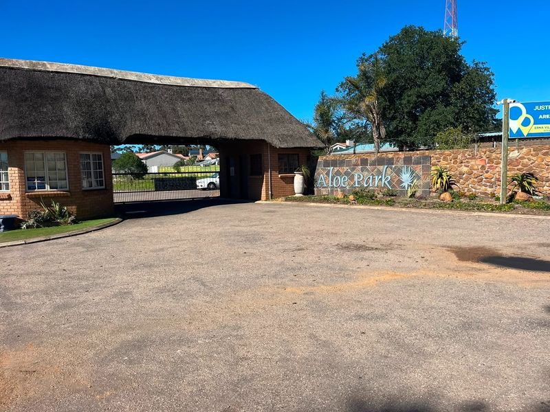 The entrance to Aloe Park featuring a thatched roof gatehouse, stone-clad signage, and a secure gated access point.
