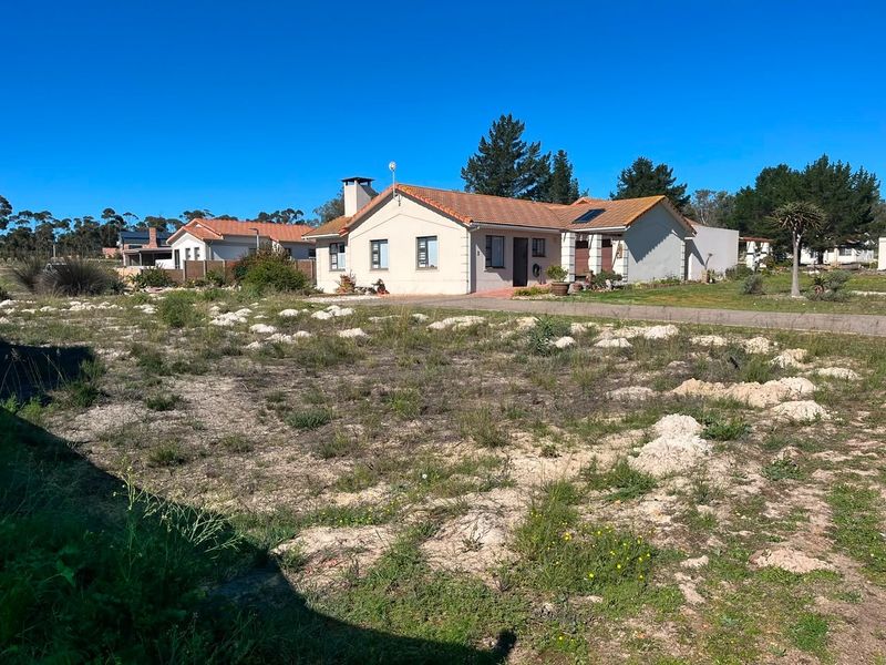 A view of a residential property featuring a tiled roof, chimney, and paved driveway, set within a spacious, undeveloped plot of land.