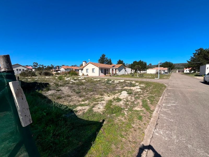 A view of an undeveloped residential plot situated along a paved street in a suburban neighborhood.