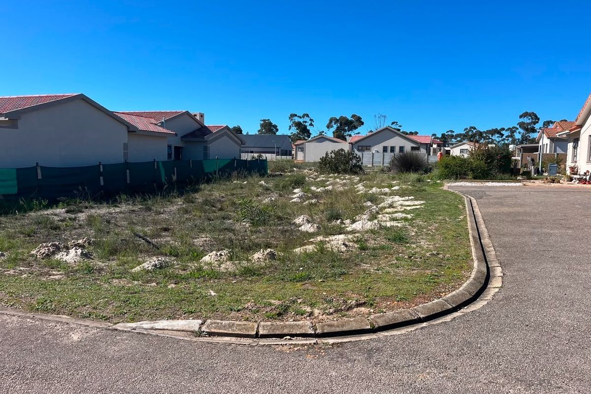 A vacant residential plot situated on a corner lot, featuring established curb infrastructure and adjacent asphalt road access in a developed neighborhood.