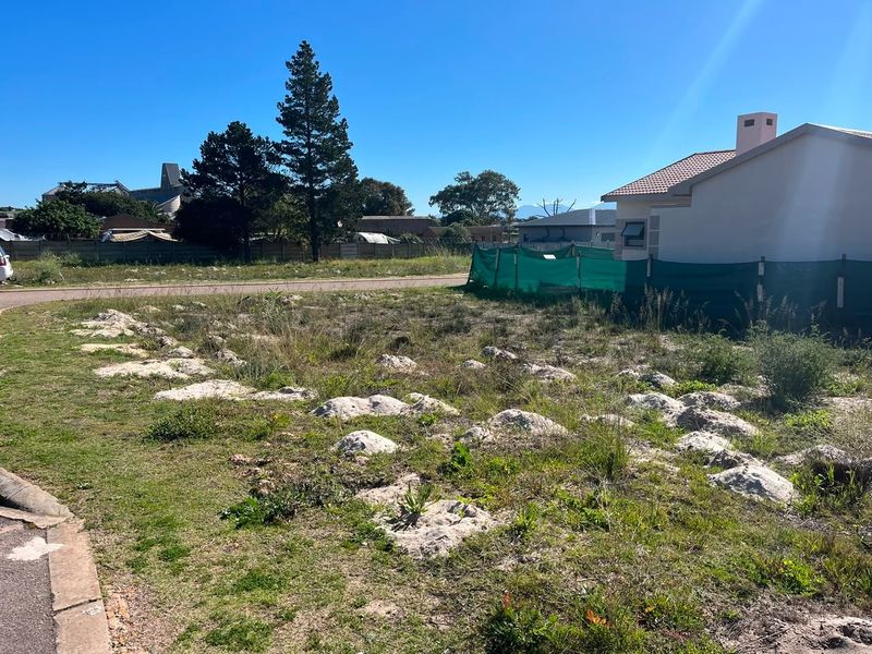 A vacant residential plot of land featuring natural ground cover and rocky outcrops, situated in a developed neighborhood setting.