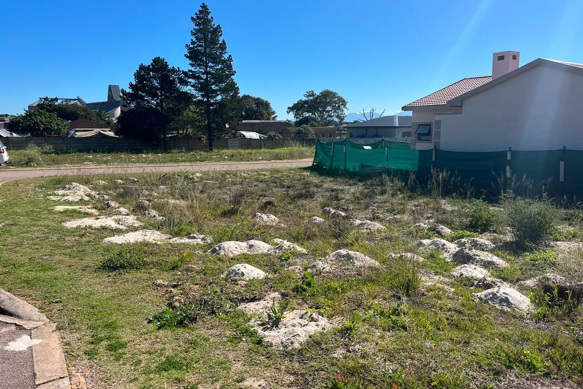 A vacant residential plot of land featuring natural ground cover and rocky outcrops, situated in a developed neighborhood setting.