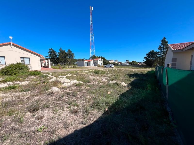 A view of an unimproved residential plot featuring natural vegetation, perimeter fencing, and a prominent telecommunications tower in the background.