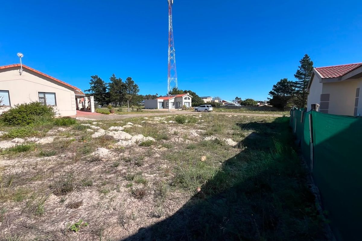 A view of an unimproved residential plot featuring natural vegetation, perimeter fencing, and a prominent telecommunications tower in the background.