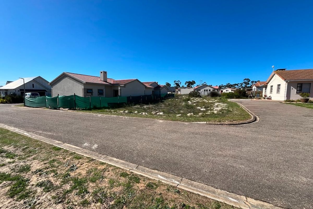 A street-level view of a vacant residential plot situated within a developed neighborhood, featuring paved road access and established surrounding homes.