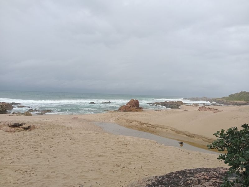 A scenic view of the sandy beach, rocky shoreline, and ocean waves under an overcast sky.