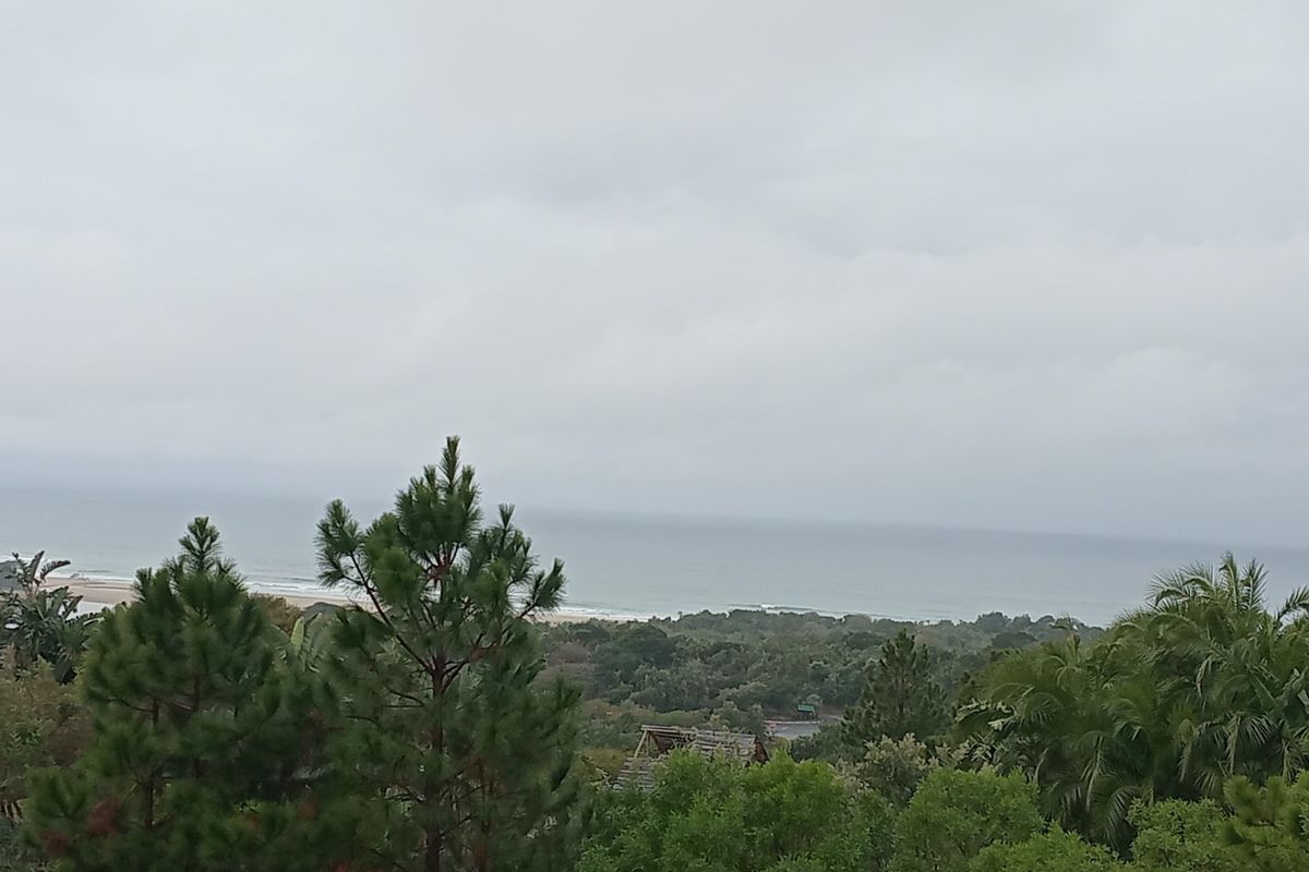 A scenic elevated view overlooking the coastal landscape, lush greenery, and the ocean horizon under an overcast sky.