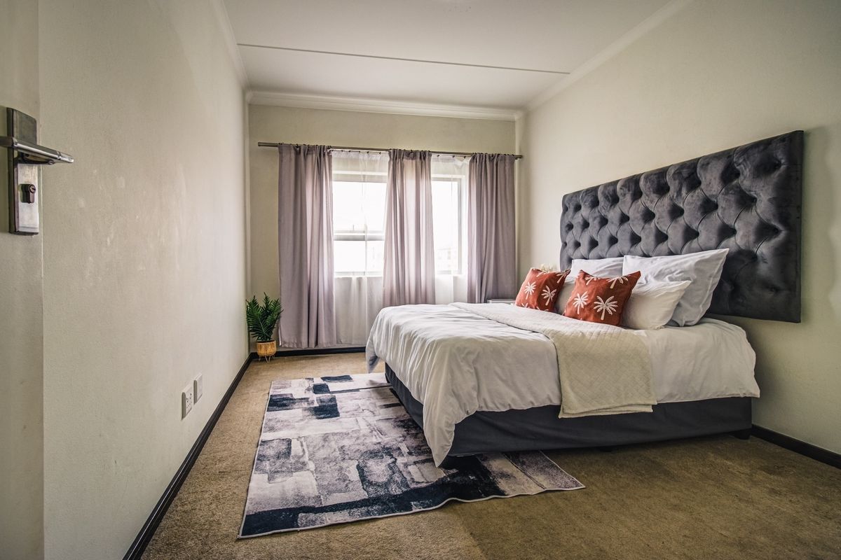 A well-lit bedroom featuring neutral walls, carpeted flooring, and a window with installed curtain rods, providing a comfortable and functional living space.