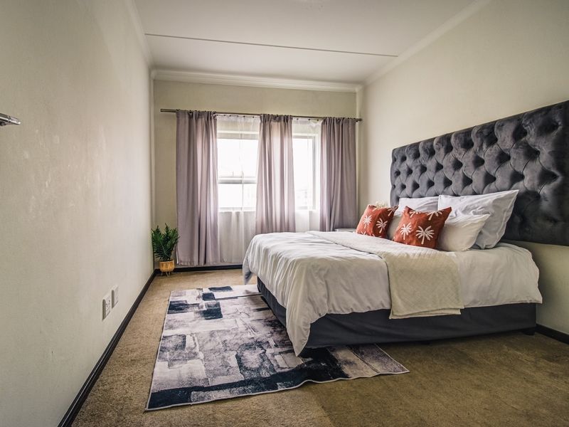 A well-lit bedroom featuring neutral walls, carpeted flooring, and a window with installed curtain rods, providing a comfortable and functional living space.