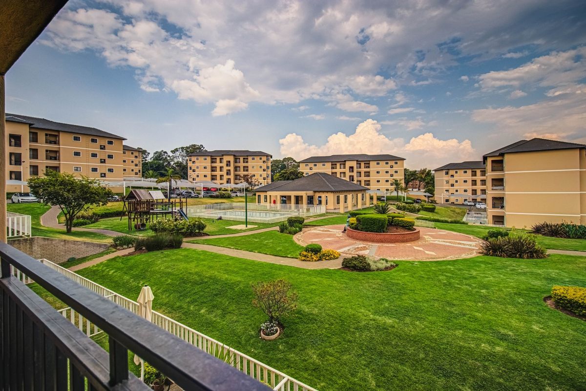 A view of the apartment complex grounds featuring landscaped gardens, paved walkways, a swimming pool, and a communal clubhouse area.