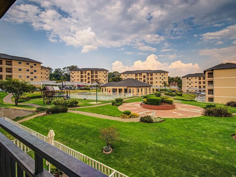 A view of the apartment complex grounds featuring landscaped gardens, paved walkways, a swimming pool, and a communal clubhouse area.