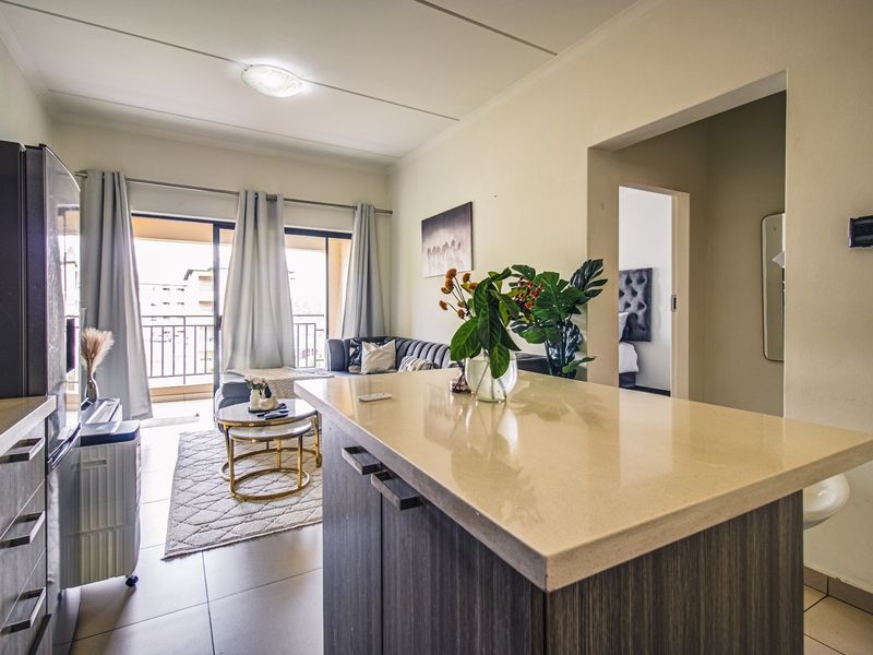 Open-plan living area featuring a modern kitchen island with stone countertops, tiled flooring, and seamless access to a private balcony.