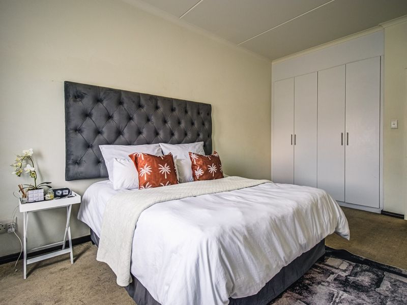 A well-lit bedroom featuring neutral walls, carpeted flooring, and ample storage provided by white built-in cupboards.