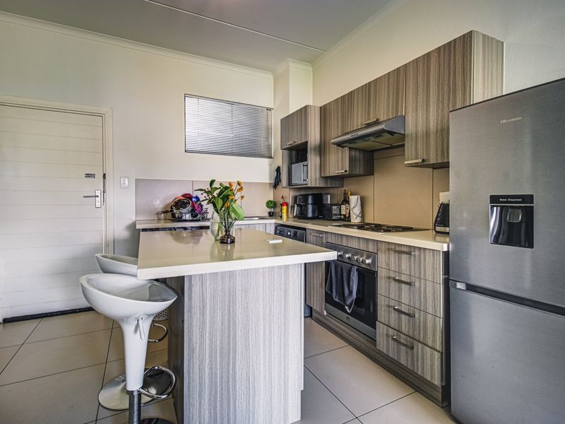Modern kitchen featuring wood-grain cabinetry, stone countertops, a central island, and integrated appliances, finished with neutral tiled flooring.